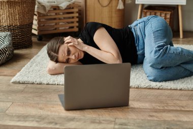 Middle aged woman laying beside laptop in distress. clipart