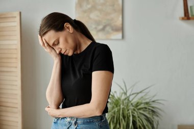 Middle aged woman in distress holds head while standing in living room.