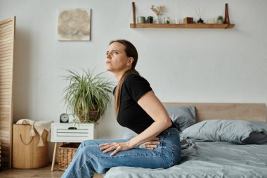 Middle-aged woman sitting on a bed, struggling with depression. clipart