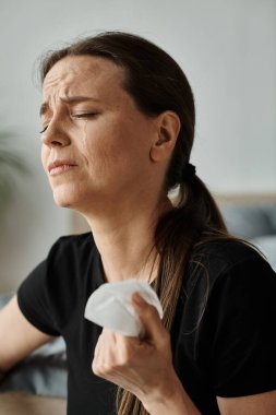 A middle-aged woman sits on a bed, holding a tissue in her hand.