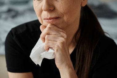 Middle-aged woman holding a tissue in her hand, showing emotional vulnerability.
