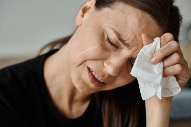 A middle-aged woman wiping her face with a tissue in a moment of vulnerability. clipart