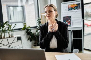 A middle-aged woman sits at a desk, staring at her laptop screen in despair. clipart