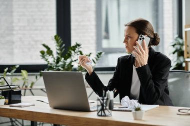 A middle-aged woman in distress talks on the phone while sitting at a desk.