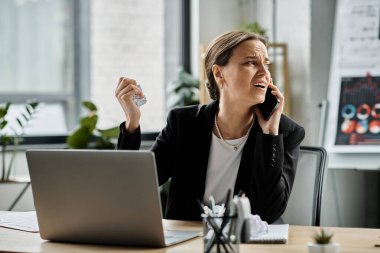 A woman in her office, absorbed in a phone call while seated at her desk.