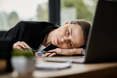 A woman with a laptop, overwhelmed on a desk.