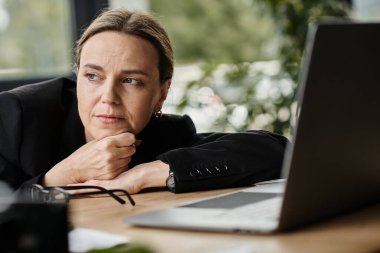 A woman gazes at her laptop on a desk.
