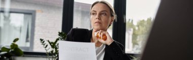 Woman sitting at window, reading paper with intense focus.