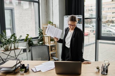 A woman standing stressed at a desk with a document in front of her.