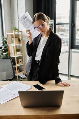 Stressed middle-aged woman in business suit sits at desk with papers. clipart