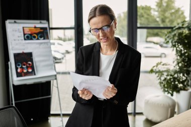 Middle-aged businesswoman experiencing stress and mental exhaustion while reviewing a document in her office.