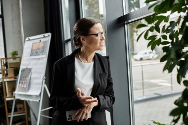 Depressed business woman standing by office window, overwhelmed by stress. clipart