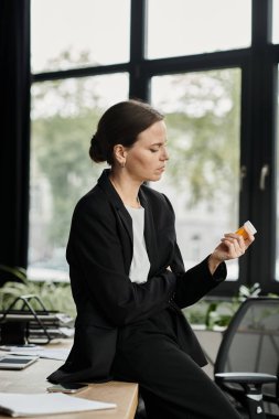 Middle aged woman at desk, staring at pills with a troubled expression.