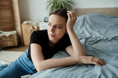 Middle-aged woman lying on bed with head in hands, showing signs of depression. clipart