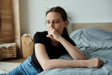 Woman in deep thought, resting on bed with chin on hand.