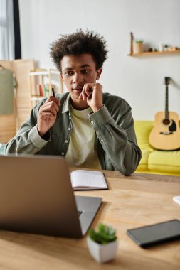 Young man, laptop on desk, studying online at home.
