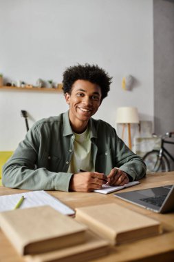 A young man, immersed in his work, sits at a desk with a laptop and a notebook. clipart