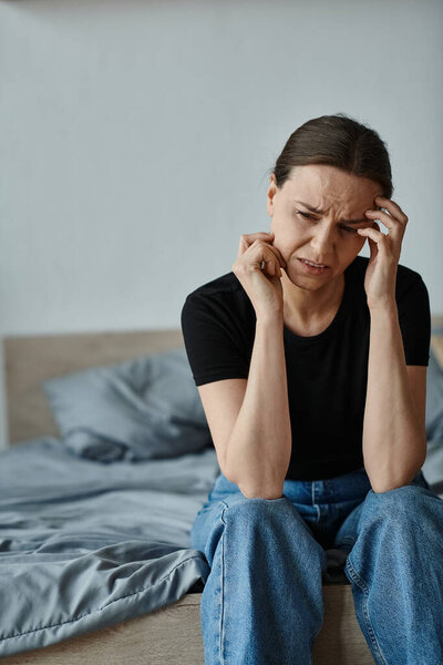 Woman in distress sitting on bed with hands on head.