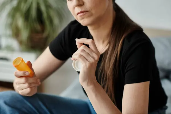 stock image A woman sits on a bed holding a bottle of medicine.