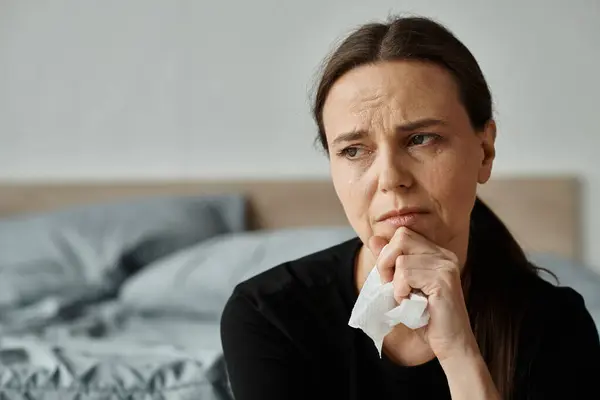 stock image A woman sits on a bed, holding a tissue.