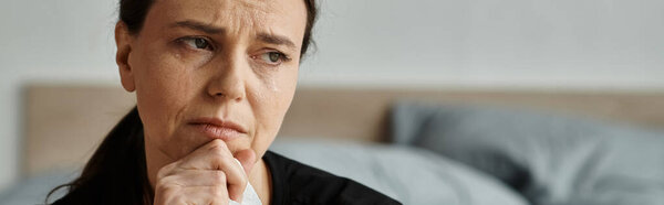Woman sitting on bed, chin on hand, struggling with depression.