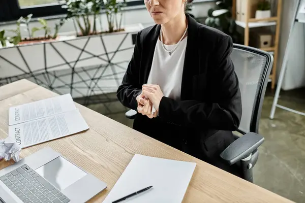 stock image A middle-aged woman sits at a desk, overwhelmed by stress while working on her laptop.