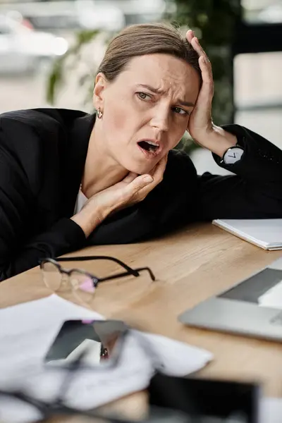 Stock image Woman sitting with hands on head, feeling overwhelmed and stressed in office environment.