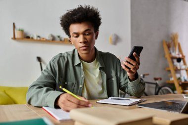 Young African American man studying at home with notebook and cell phone.