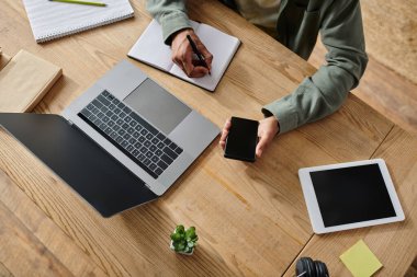 Young African American man studying online at home with laptop and cell phone on desk.