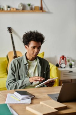 Young African American man focusing on laptop screen while studying at home.