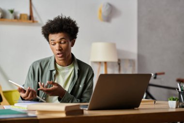 Young man engrossed in online studies on laptop and cell phone.