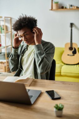 A young African American man studying online with headphones and laptop at home.