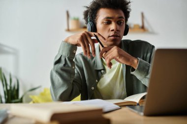 A young African American man is focused on his laptop, studying online while wearing headphones.