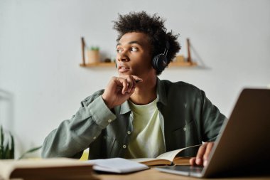 A young man of African American descent wearing headphones, deeply focused while sitting at his desk with a laptop.