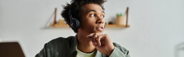 A young man, wearing headphones, focused on his laptop screen.