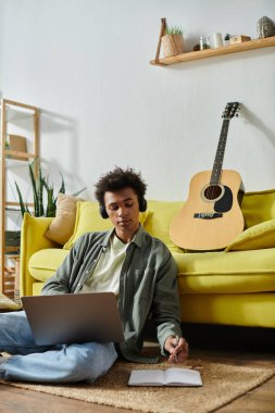 A young man, headphones on, strums a guitar on a yellow couch.