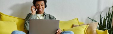 A young African American man studying online with a laptop on his lap.