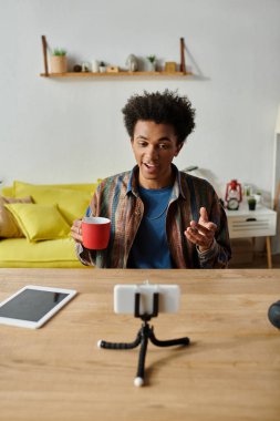 Young African American male blogger chatting on phone camera while savoring a cup of coffee.