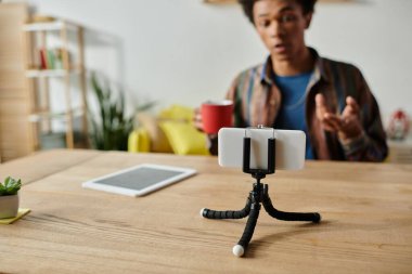 Young African American male blogger recording himself on phone on tripod.