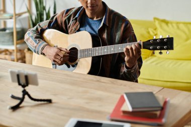 A young African American man passionately playing an acoustic guitar at home.