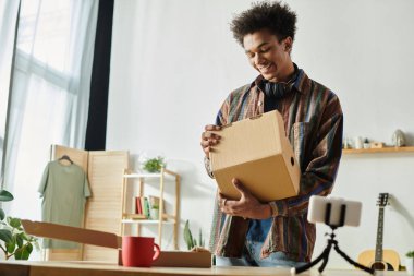 A young Black man displays a cardboard box in front of a desk. clipart
