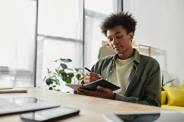 Man of African descent sitting at desk, focused on writing in notebook.