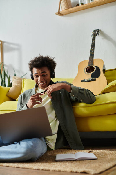 Young man with headphones and guitar seated on floor.