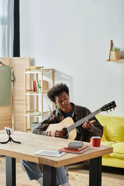 stock image A man of African American descent sits at a table, engrossed in playing an acoustic guitar.