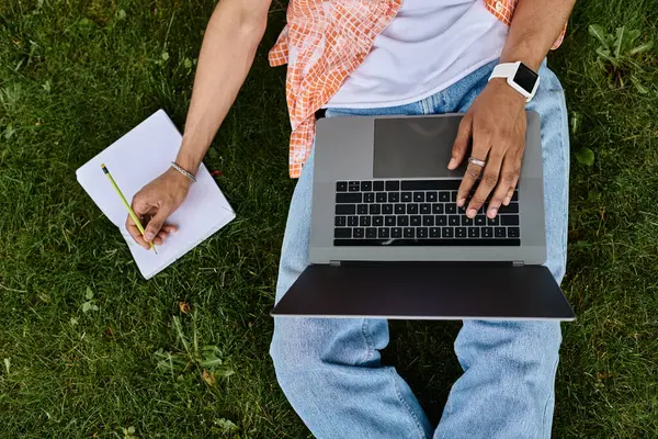 stock image man working outdoors with laptop and notebook on grass.