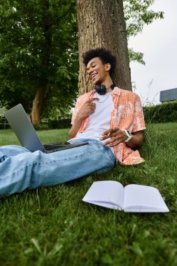 Young man enjoys music and works on laptop in grass.