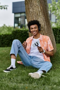 A young man sitting on grass next to a tree in the park.
