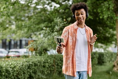 A young African American man lost in his phone amidst the serene park surroundings.