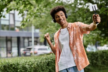 A young African American man happily taking a selfie in a vibrant park setting.