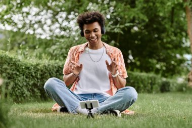 Young man, African American, seated on grass, engaged in phone conversation.